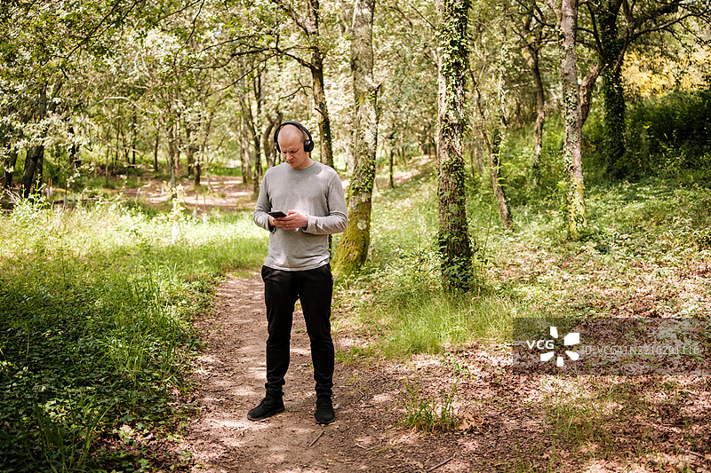 在森林中，男子戴着耳机听音乐并使用智能手机图片素材