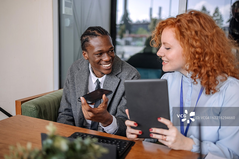 女商人在咖啡馆与客户会面，讨论金融贷款，而客户正在通过手机与第三方咨询。图片素材