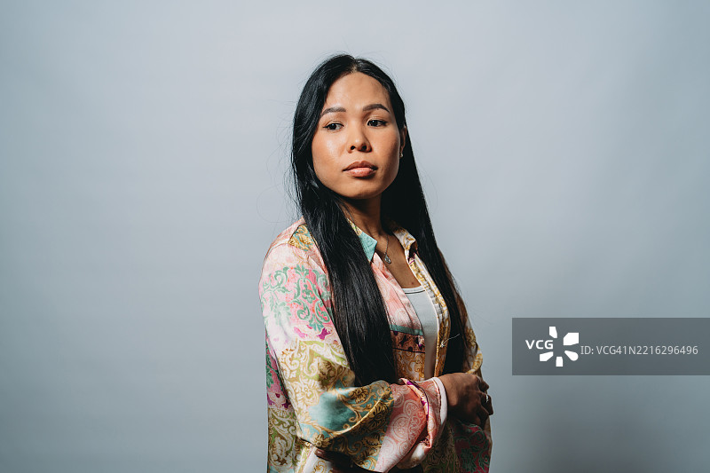 年轻亚洲女性在灰色背景前摆姿势，双臂交叉。图片素材