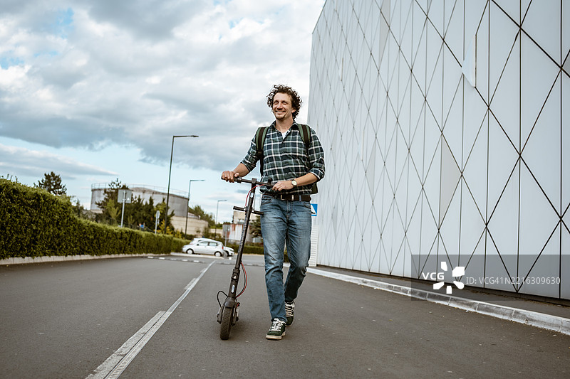 男子在阴天的城市环境中骑电动滑板车行走图片素材