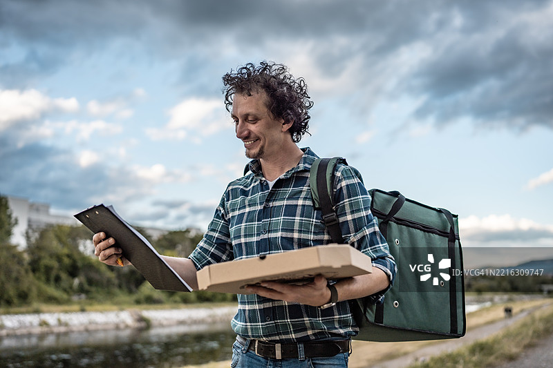 户外环境中手持食品包和清单的送货员图片素材
