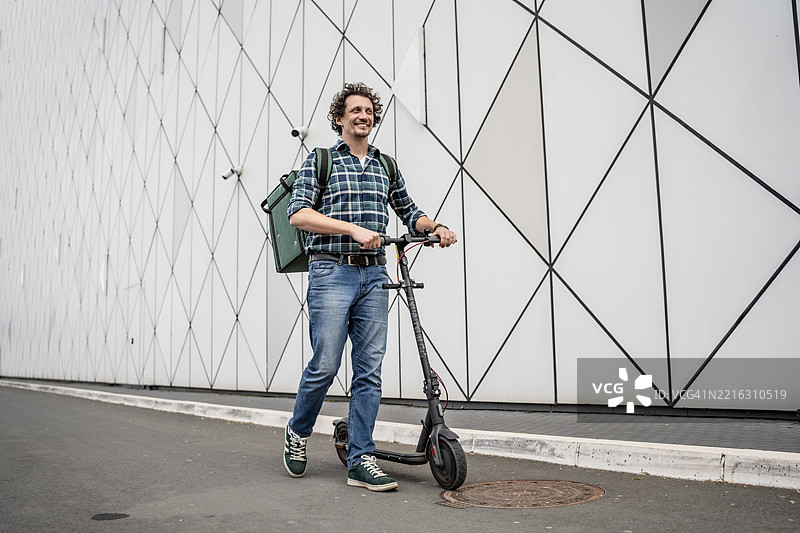 微笑的男子在现代背景下骑着电动滑板车穿行于城市环境中图片素材