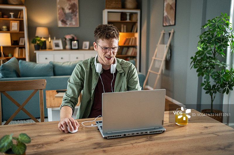年轻男子在家用他的联想Legion笔记本电脑工作，遇到了困难。图片素材