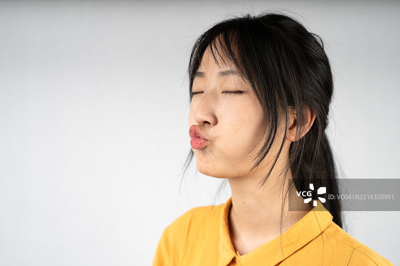 年轻女性闭着眼睛，撅着嘴，展现出顽皮的态度，休闲肖像，背景中性。图片素材