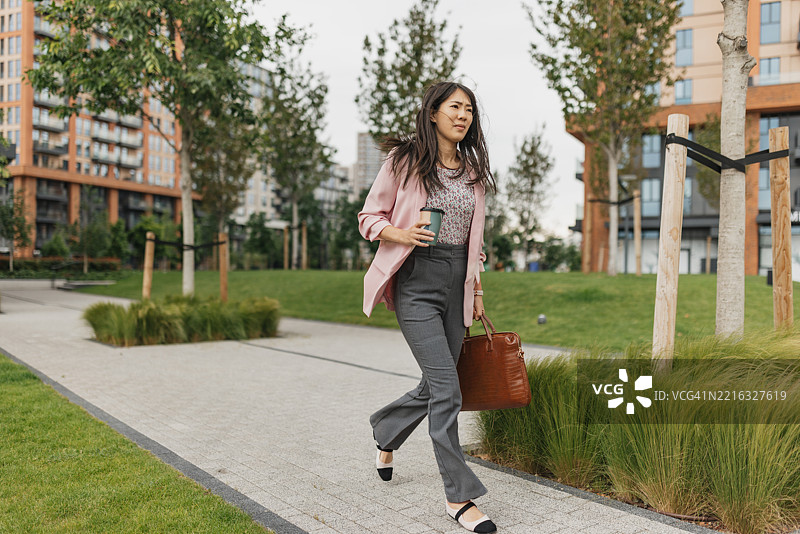 女商人在走路时享受咖啡图片素材