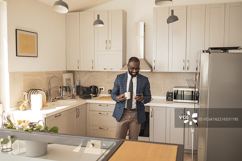 专业男士在时尚厨房中手持咖啡杯和智能手机图片素材