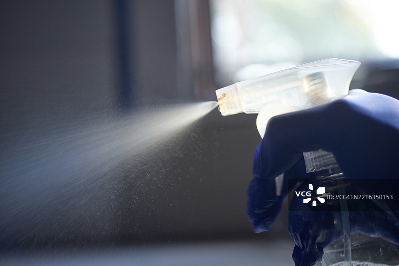 戴着保护手套的人在喷洒消毒液，彻底清洁表面，消灭细菌，保持卫生的工作环境。图片素材