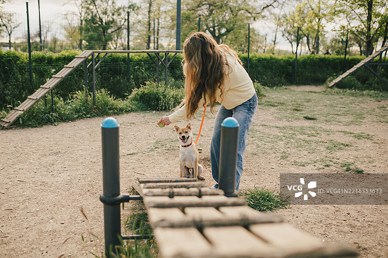 阳光明媚的日子里，女人在户外敏捷训练公园训练她的狗图片素材
