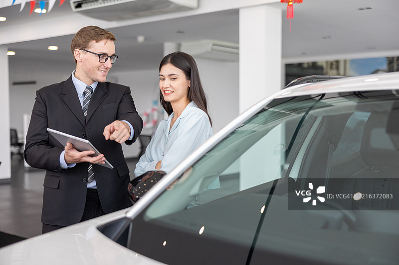 新车购买体验：白人销售员在明亮现代的汽车展厅中为女性顾客提供详细的汽车介绍和专业咨询，以便顺利决策。图片素材
