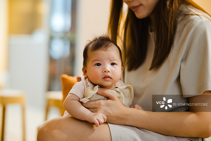 亚洲母亲在家中用手帮助婴儿打嗝，缓解喂养后的不适。图片素材