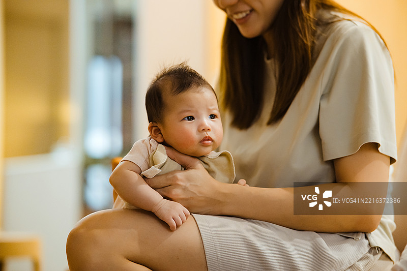 亚洲母亲在家中用手帮助宝宝打嗝，缓解喂养后的胀气。图片素材