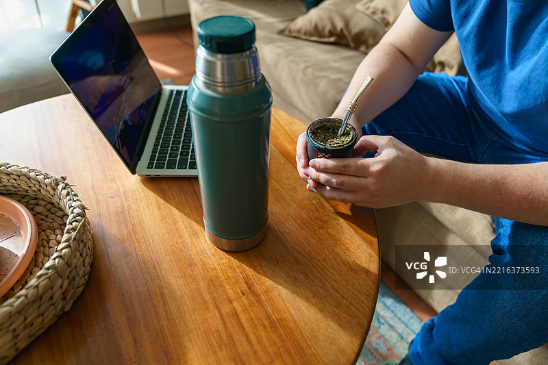 年轻人坐在桌子旁喝马黛茶，桌上放着笔记本电脑图片素材