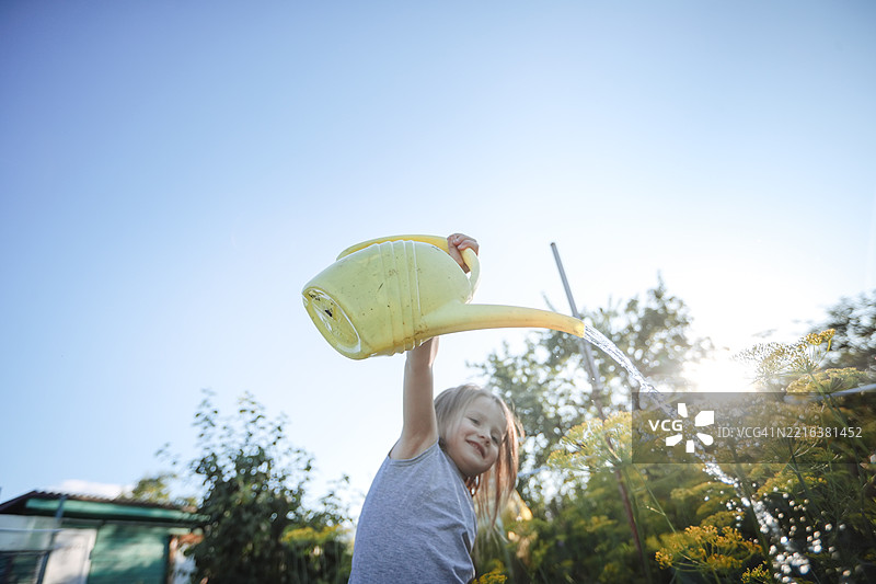 充满活力和快乐的女孩用黄色的浇水壶关注她的花园，低角度拍摄。图片素材