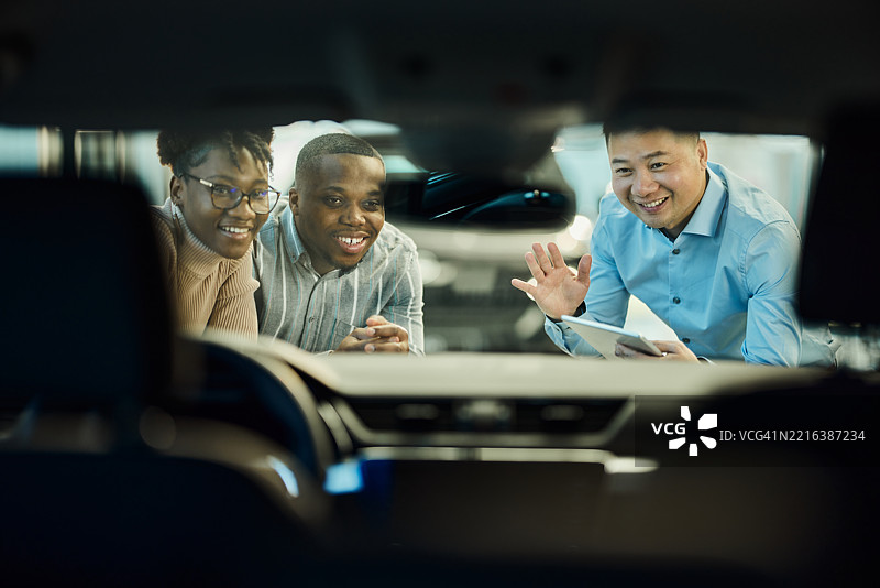 快乐的亚洲销售员在展厅里向一对黑人夫妇出售汽车。图片素材