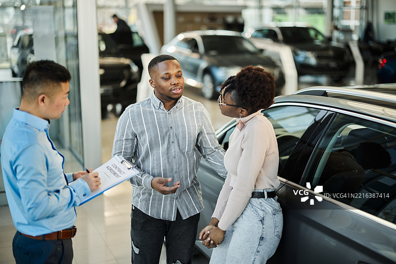 一对黑人夫妇在展厅里与汽车销售员交谈。图片素材