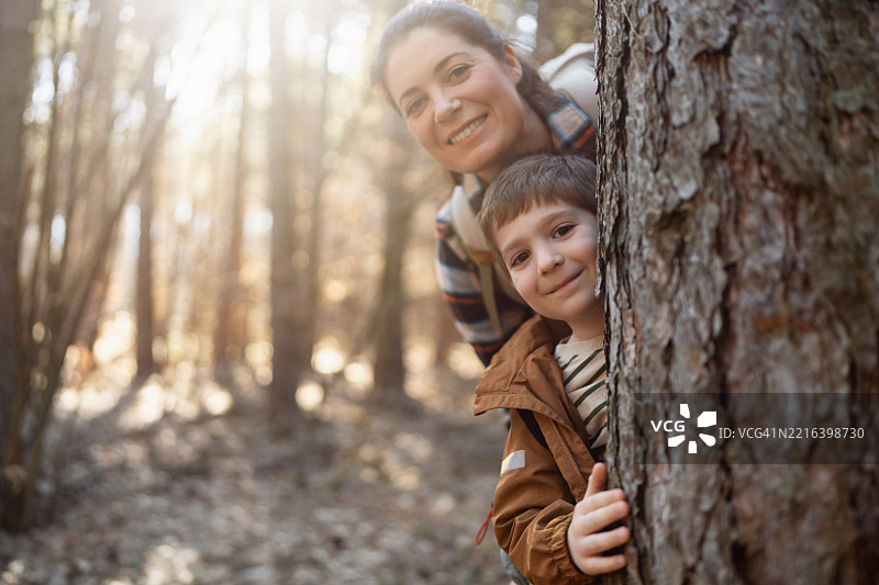 妈妈和儿子从树后探出头来，拍摄有趣的肖像照图片素材