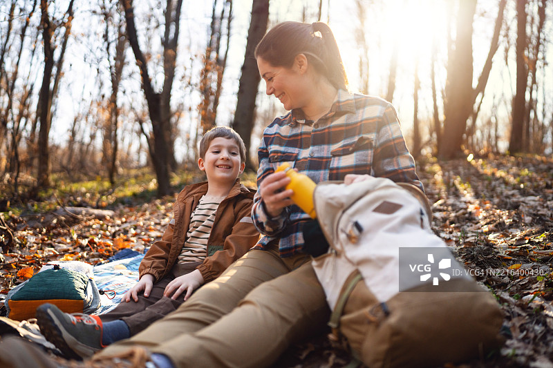 妈妈和她的儿子在徒步旅行中休息，悠闲地坐在宁静的森林里的毯子上。图片素材