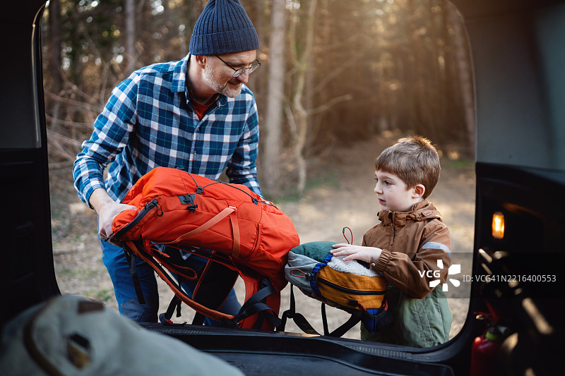 父亲和他的儿子正在从汽车后备厢中取出登山装备，准备开始他们的户外冒险。图片素材