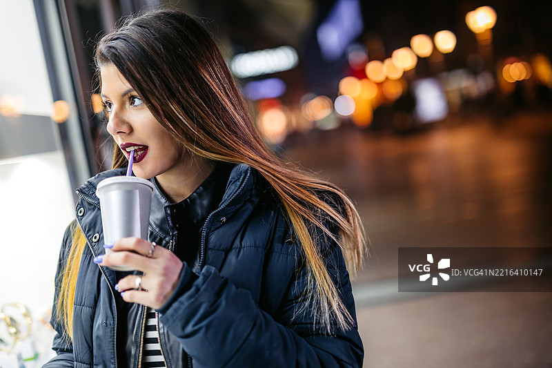 年轻女性在冬季夜晚户外逛街时喝奶昔图片素材