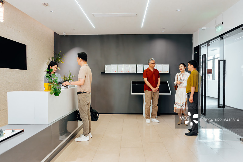 亚洲商人到达办公室，与同事交谈。他正在使用智能考勤机。图片素材