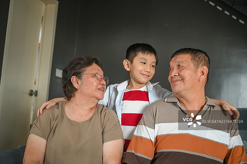 快乐的时刻，亚洲祖父母和他们的孙子坐在家里的沙发上。图片素材