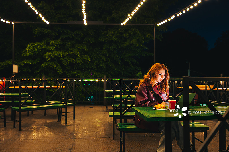 夜晚在空荡荡的咖啡馆里，女性在笔记本电脑上远程工作图片素材