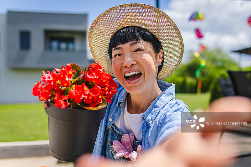 日本女性园丁在后院与红色盆栽花卉自拍的肖像图片素材