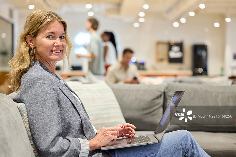 微笑的女商人坐在沙发上使用笔记本电脑图片素材