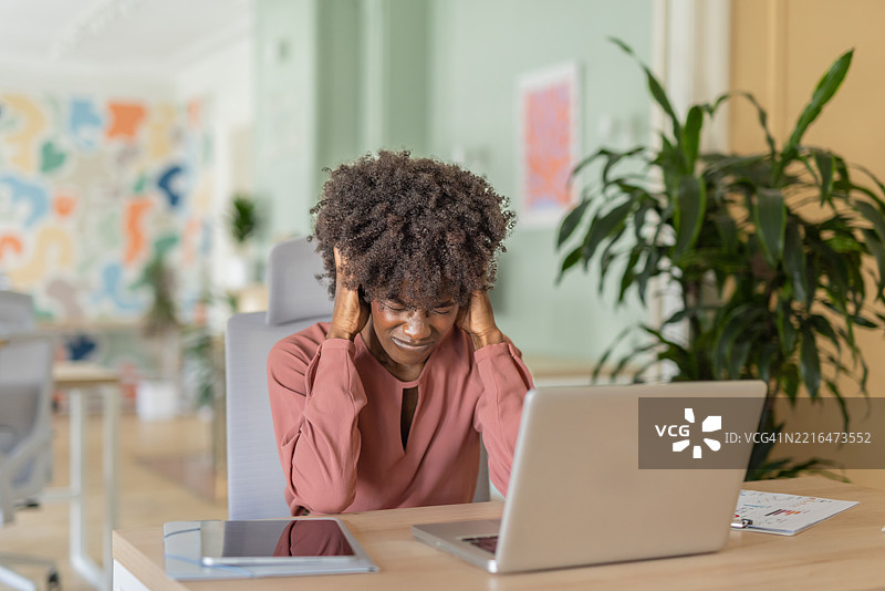 压力大的女性在笔记本电脑桌前工作，留着自然卷发图片素材