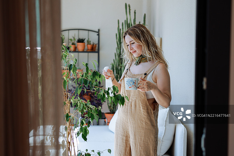 成年女性用白色喷雾瓶给室内植物喷水图片素材