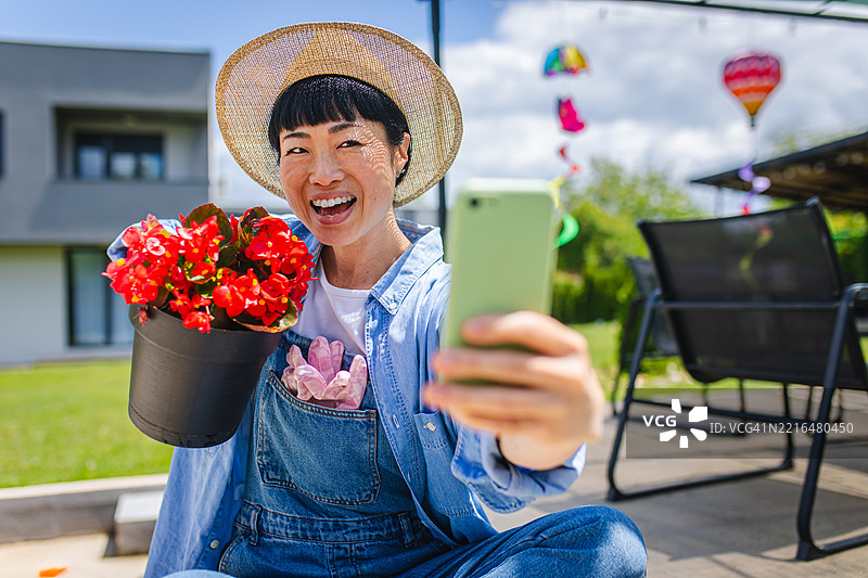 日本女性园丁在后院与红色盆栽花卉自拍图片素材