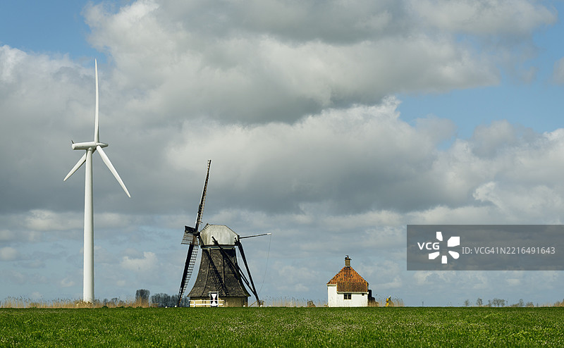 荷兰乡村中一座传统与现代风车，旁边有一座农舍，天空多云。图片素材