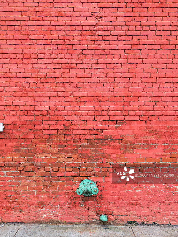 红色涂漆和风化的砖墙，配有消防立管和喷淋头。混凝土人行道。阳光。自然色彩。猎人点（长岛市），纽约市，美国。图片素材