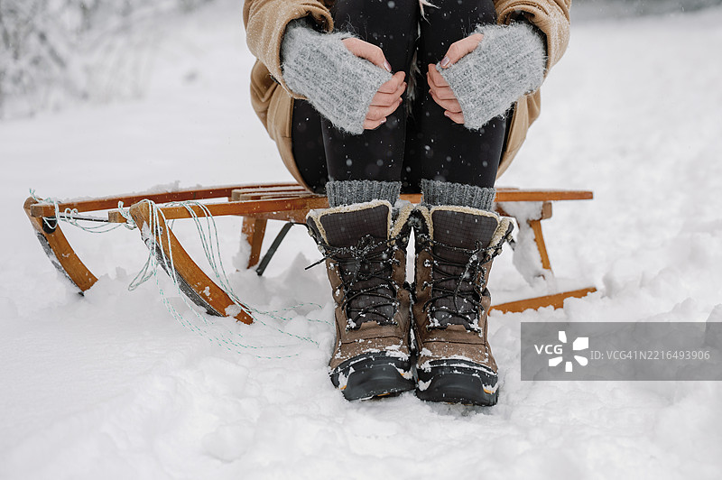 成熟的女性坐在雪地里的木制雪橇上，穿着温暖的衣服和灰色手套图片素材