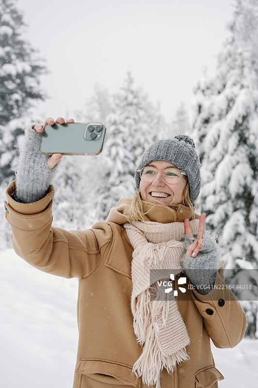 穿着冬季服装的年长女性在雪-covered户外森林中自拍图片素材