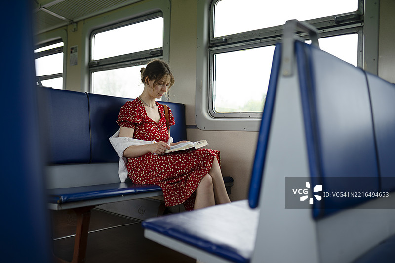 白天，一位女性在蓝色座椅的火车上阅读一本书。图片素材