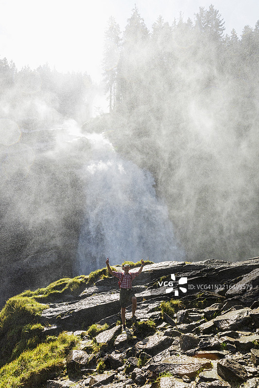 在奥地利霍赫陶恩国家公园的克里姆尔瀑布喷雾中，登山者在岩石上欢呼图片素材