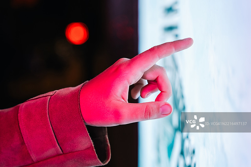 一个手指触碰着发出柔和蓝光的数字屏幕，屏幕边缘有霓虹粉色的袖子。这个手势象征着现代互动、选择和智能界面。图片素材