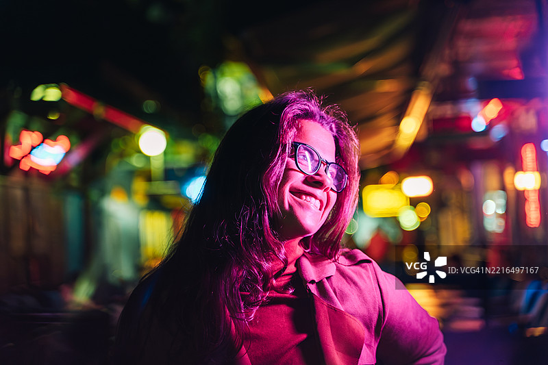 一位女性在五彩斑斓的夜景中仰望，脸上映出粉色的倒影。图片素材