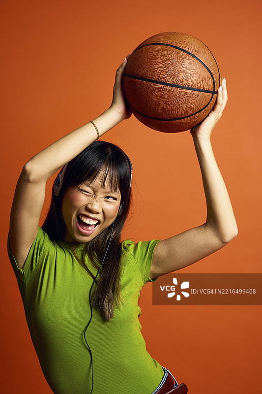 快乐的女性戴着耳机，手里拿着篮球，背景为橙色。图片素材