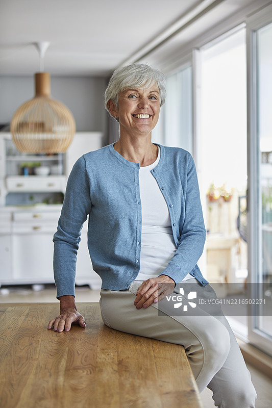 微笑的女性坐在明亮厨房的木桌上图片素材
