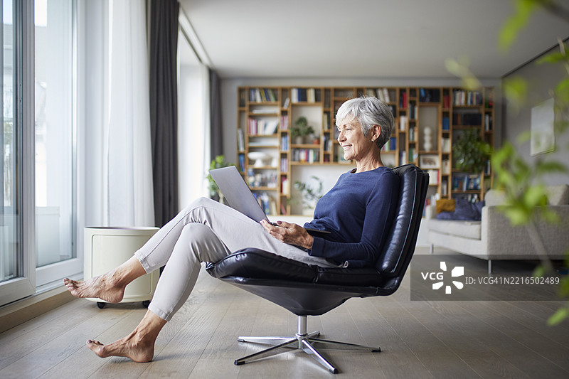 女性在现代客厅中使用笔记本电脑放松。图片素材