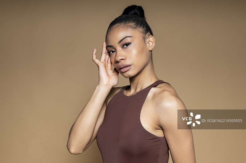 模特在米色背景的摄影棚中摆姿势，注视着镜头图片素材