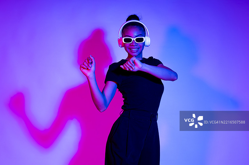 在霓虹灯下的舞蹈室里，女人戴着无线耳机和太阳镜跳舞图片素材