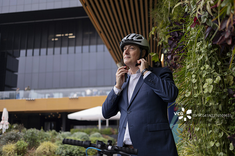 戴着头盔的商人准备骑滑板车，旁边是垂直花园。图片素材