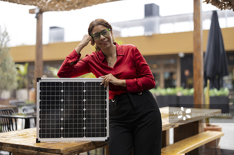 穿着红色衬衫的女性在户外靠着太阳能板，宣传可再生能源图片素材