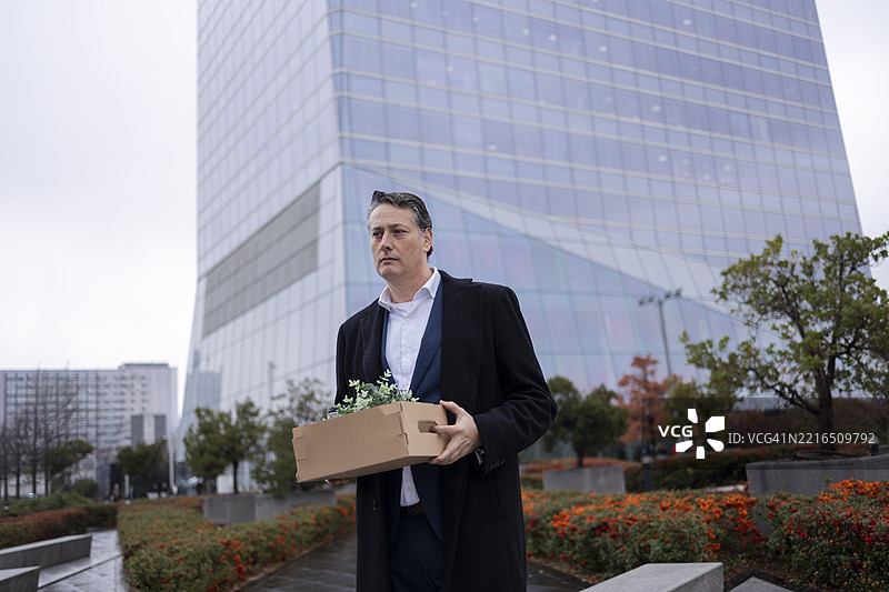 男人在摩天大楼外拿着一个纸箱，失业后显得很伤心。图片素材