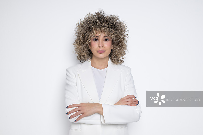 穿着白色西装、自信地在摄影棚中摆姿势的卷发女商人图片素材