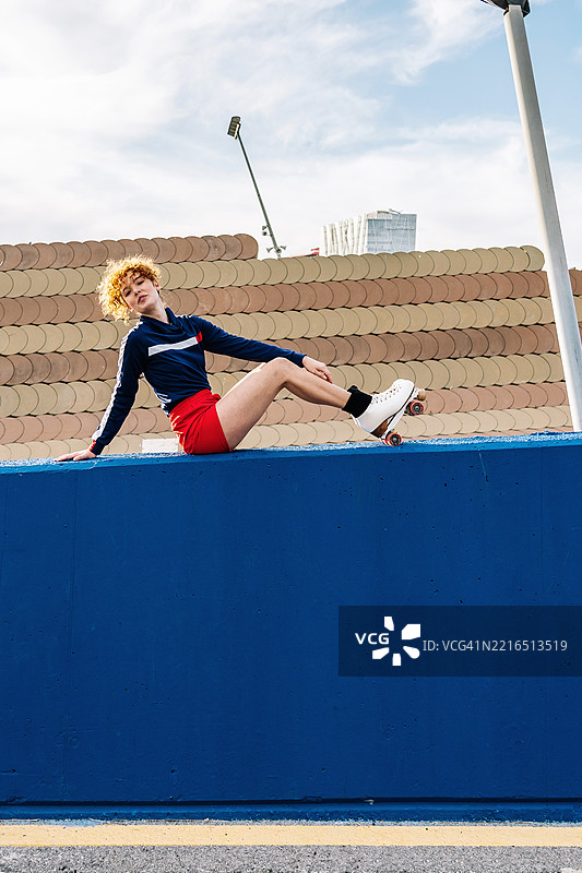 穿着滑轮鞋的女性坐在城市环境中的蓝色墙壁上图片素材