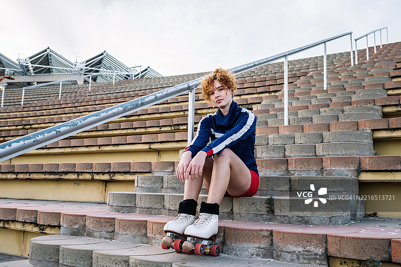 穿着轮滑鞋的卷发女性坐在户外的楼梯上图片素材